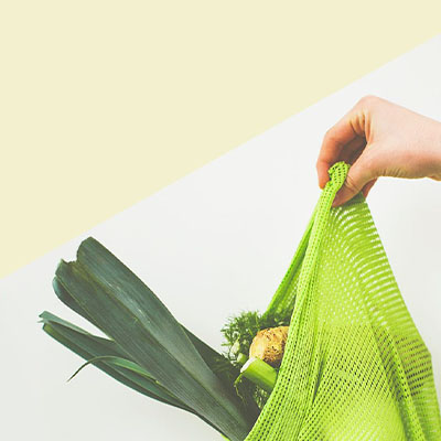 a hand holding a shopping bag filled with vegetables and healthy food