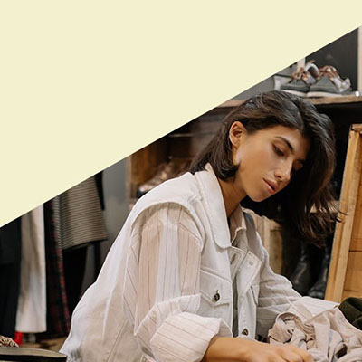a woman on her knees, looking inside a box full of second-hand clothes